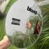 A round mirror displaying the 'Blond' logo and Frank Ocean's artwork, showcased on a modern tabletop